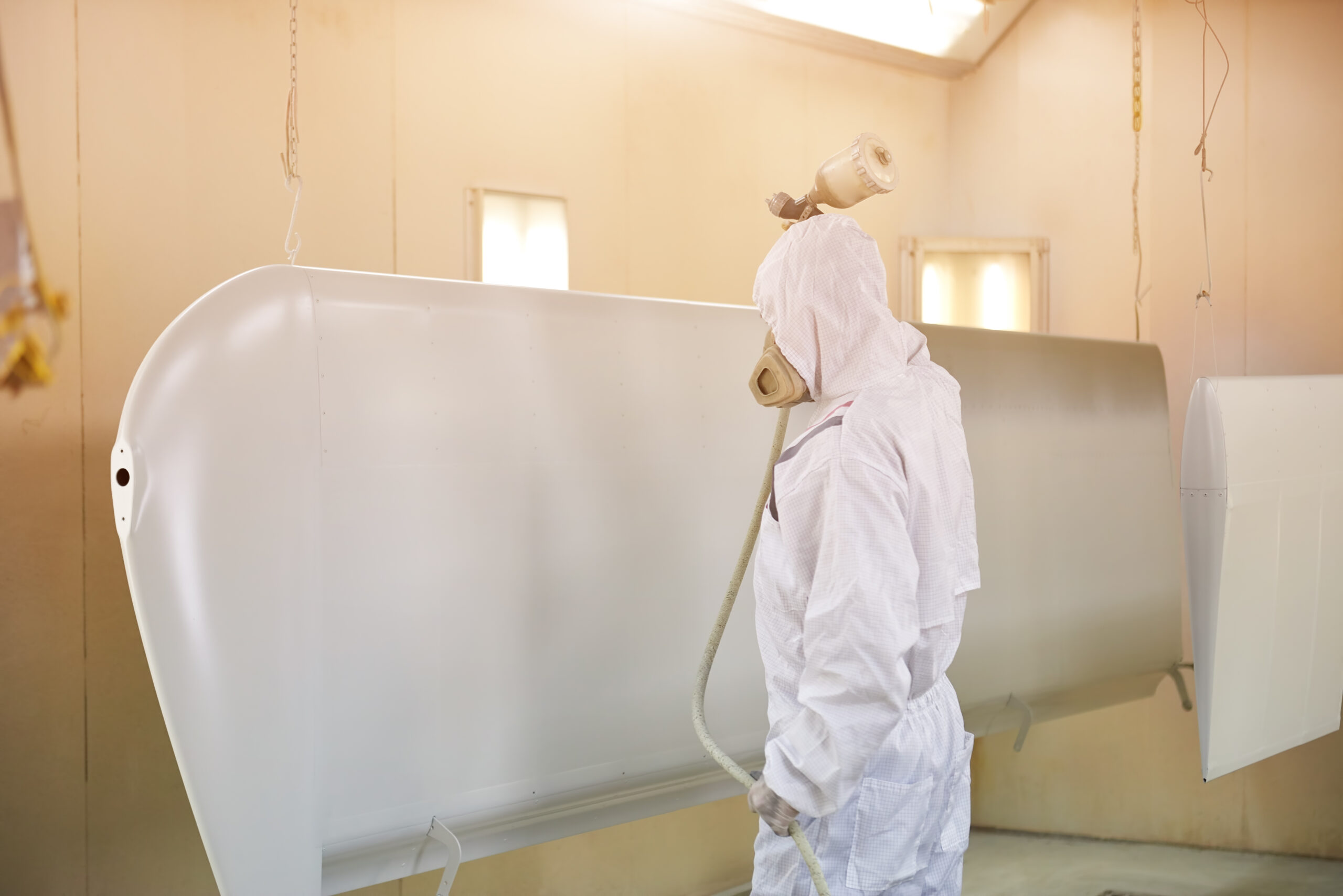 Airplane wing, spray painting. Worker in coverall.